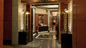 Entrada de un hotel con un piso de mármol pulido, un mostrador de recepción y dos lámparas decorativas.