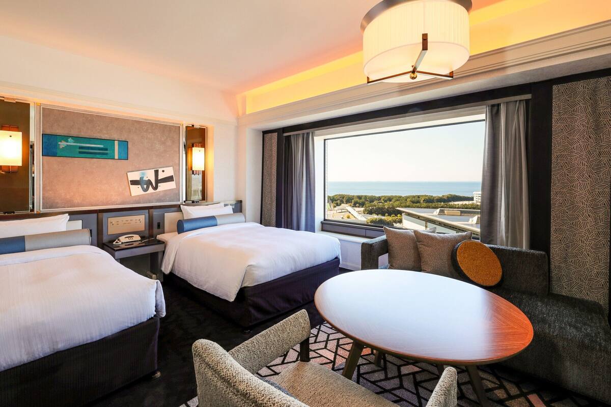 Een hotelkamer met twee bedden, een tafeltje en uitzicht op de stad.