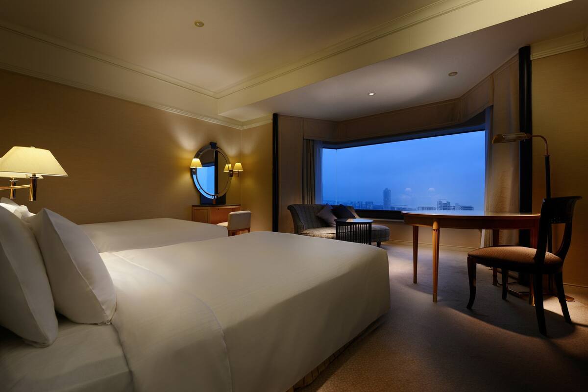 Een hotelkamer met een groot bed, een bureau, een stoel en uitzicht op de stadsgezicht door een groot raam.