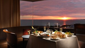 Mesa dispuesta para la cena con vistas al atardecer, incluyendo una botella de champán, copas de vino y varios platos.