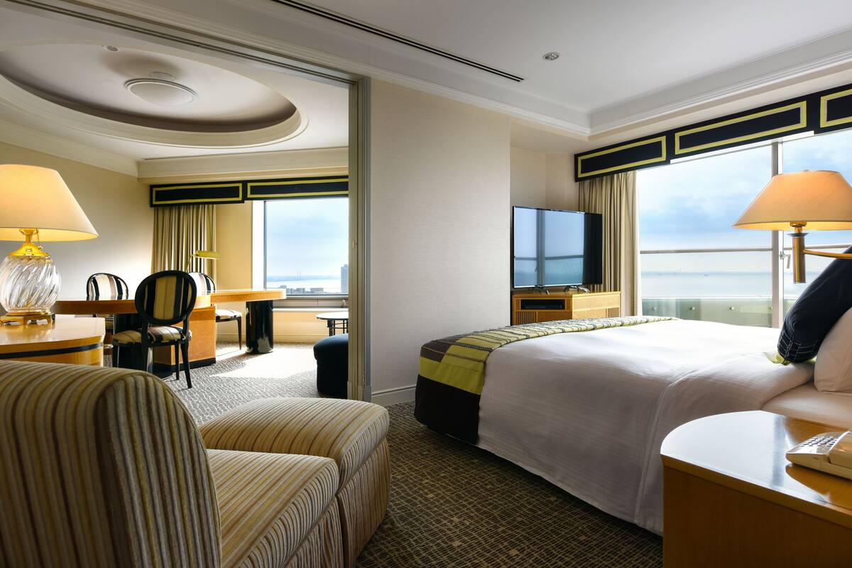 Hotelkamer met een groot bed, een bureau met lamp, een stoel, een televisie en uitzicht op de stad.