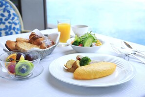 A breakfast setting with croissants, fruit, a salad, and an omelette on a table. - Hotel New Otani Makuhari (Chiba)