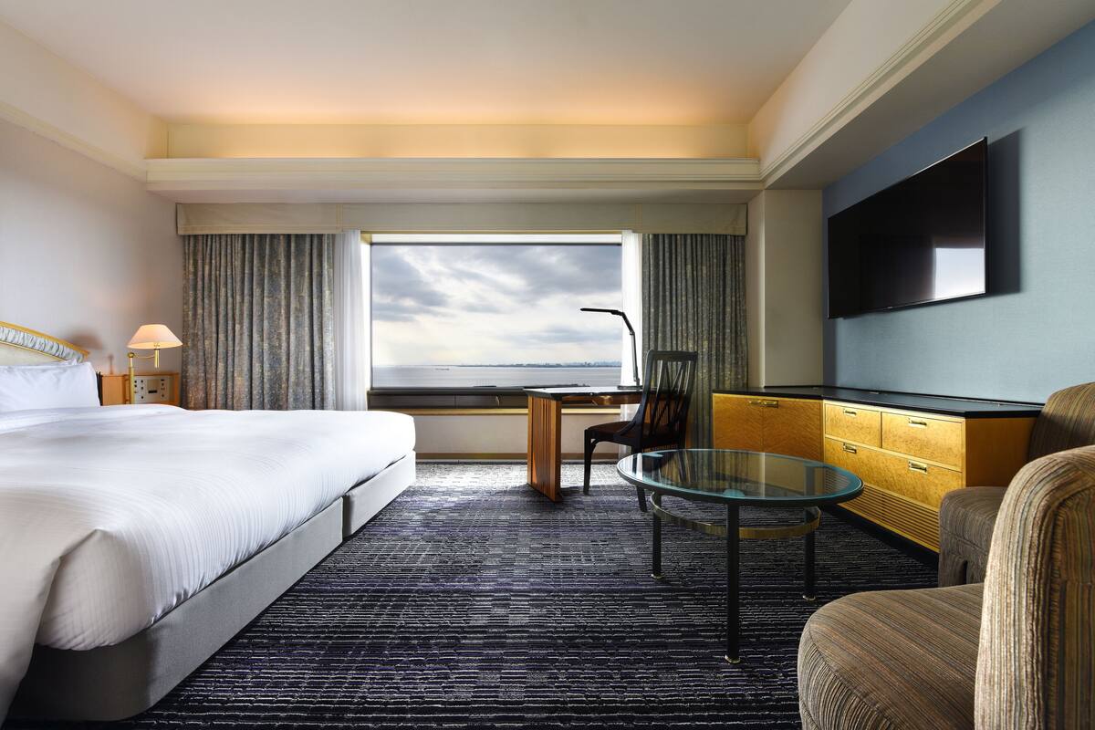 Een hotelkamer met een groot bed, een bureau met stoel, een televisie en uitzicht op de stad.