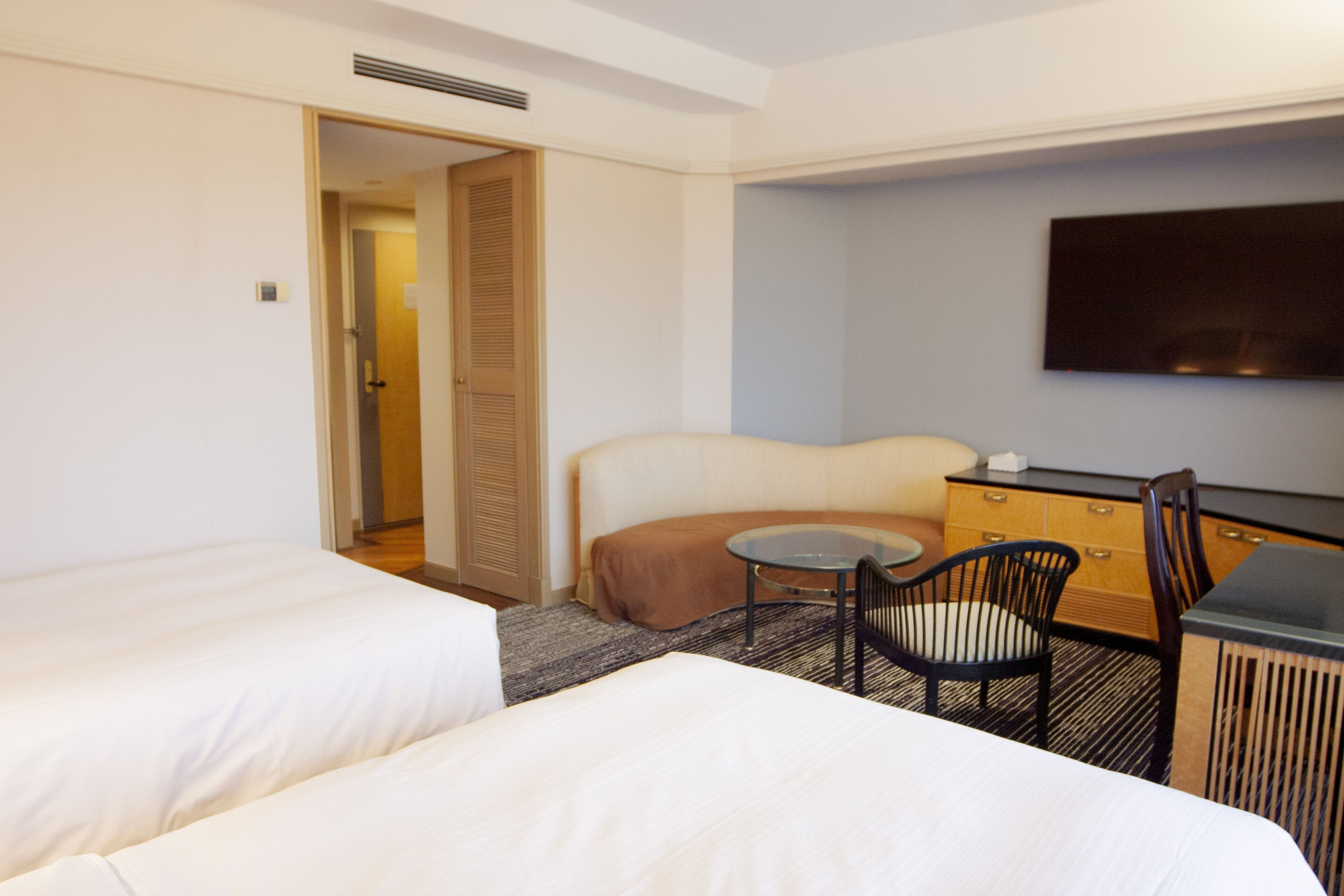 Habitación de hotel con dos camas, una mesita redonda pequeña, una silla, un televisor y un armario.