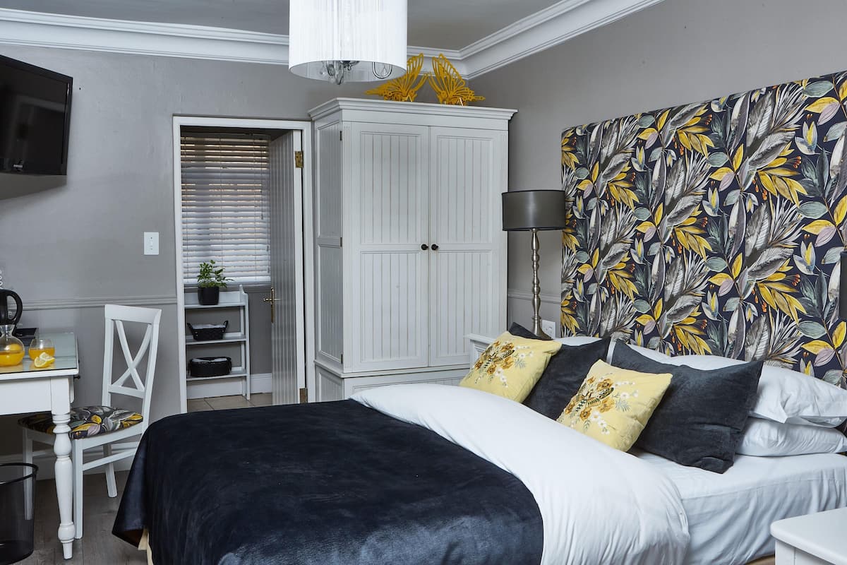 A bedroom with a bed, a wardrobe, a desk with a chair, and a television.