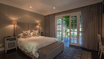A spacious bedroom with a large bed, two bedside lamps, a nightstand, and a view of the outdoors through a sliding glass door.