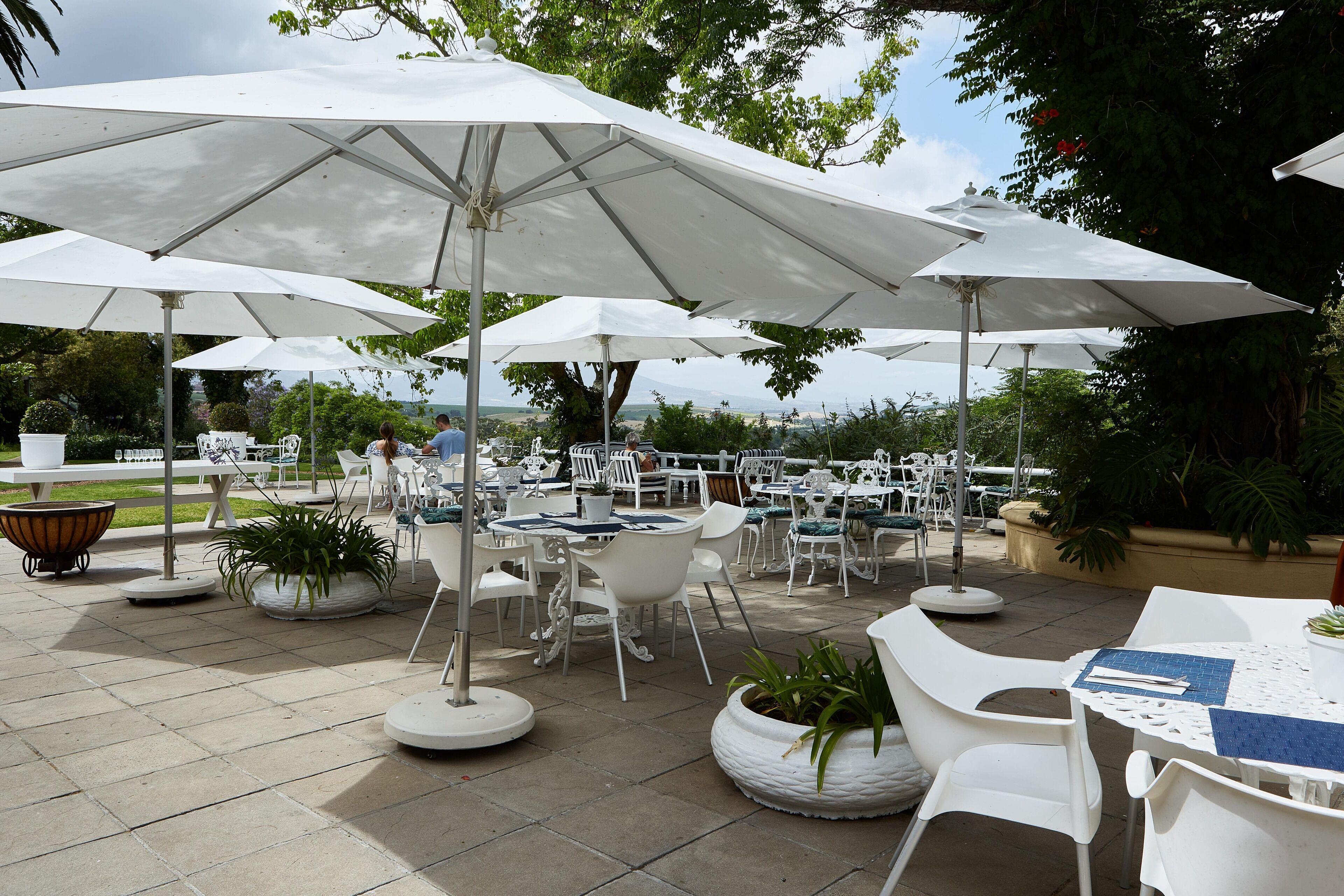 Un patio al aire libre con mesas y sillas blancas, rodeado de grandes sombrillas blancas.