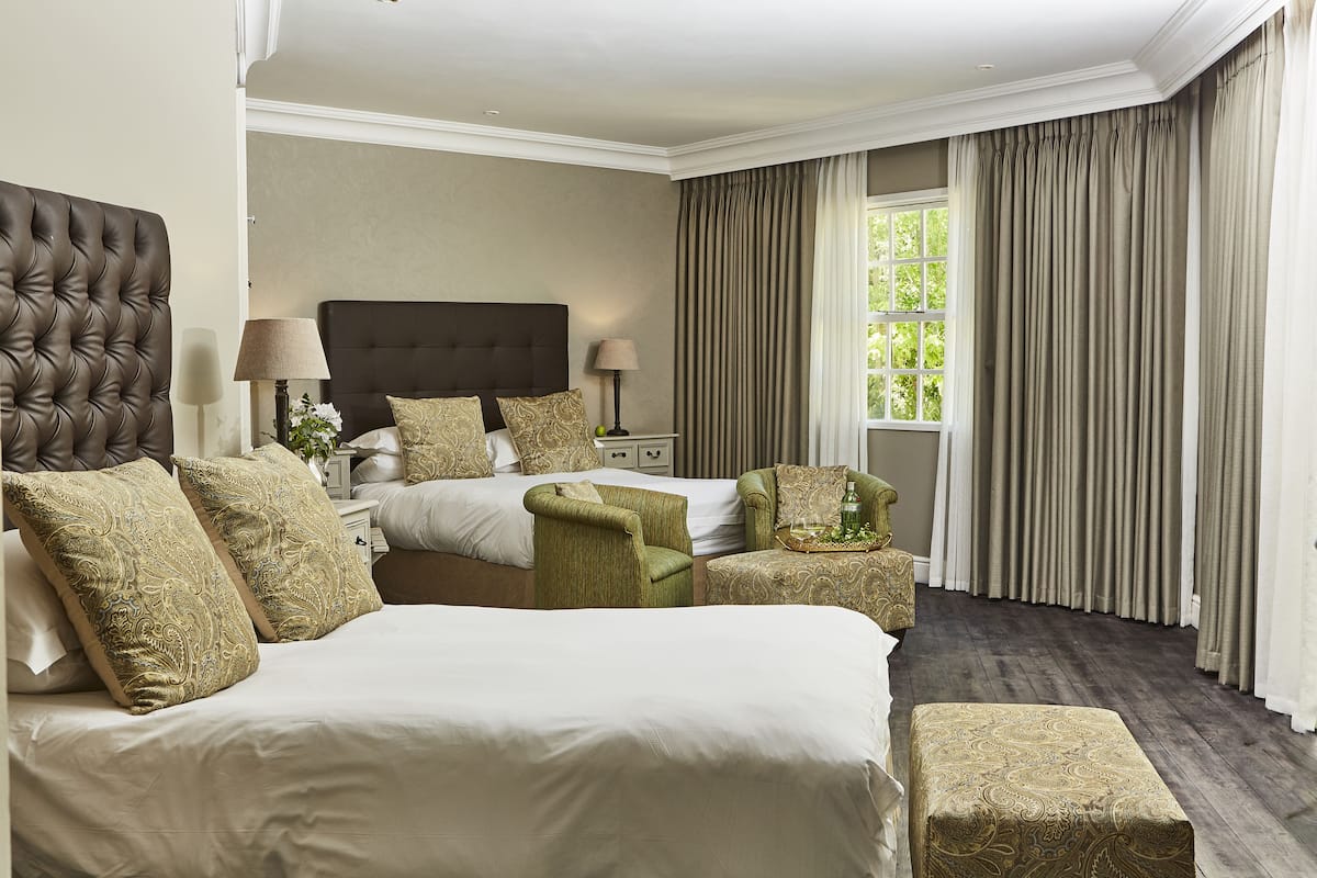 A hotel room with a large bed, two armchairs, a nightstand with lamps, and a window with curtains.