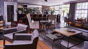 A spacious living area with multiple seating options, a coffee table, and a bar area with shelves of bottles. - The Devon Valley Hotel (Stellenbosch)