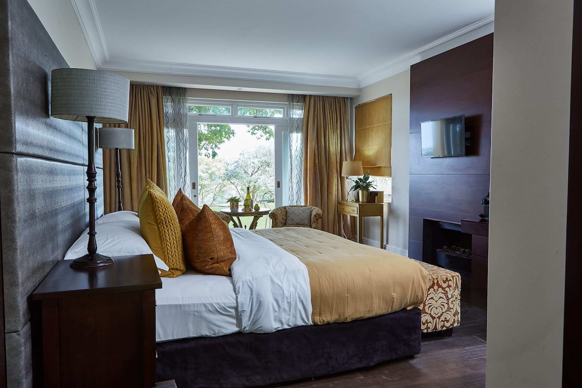 A hotel room with a large bed, a bedside table with a lamp, a TV mounted on the wall, and a view of the outdoors through the window.