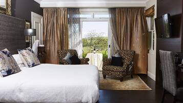 A hotel room with a large bed, two patterned armchairs, a small table, and a TV mounted on the wall.