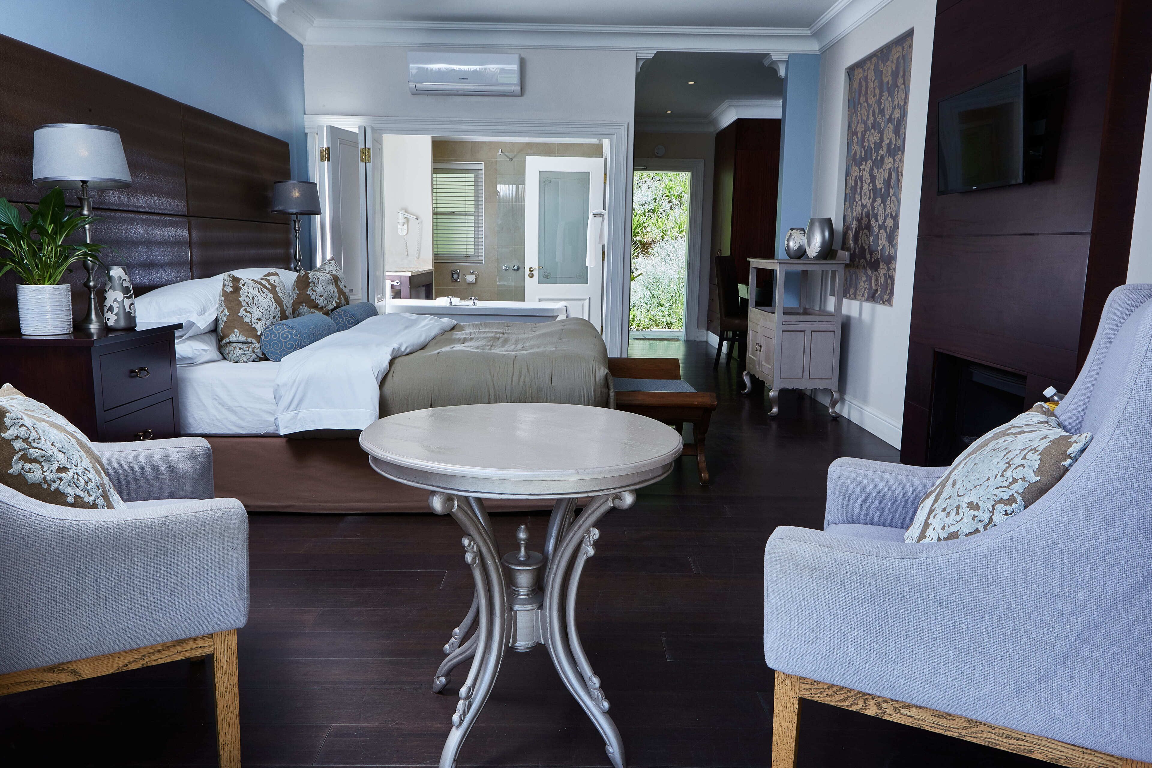 A modern bedroom with a large bed, a round table, two armchairs, and a fireplace.