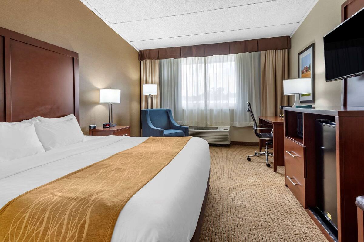 A hotel room with a large bed, a desk with a computer, a chair, and a TV.