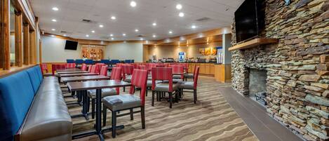 A restaurant with booths and tables, a stone wall with a fireplace, and a flat-screen TV mounted on the wall.