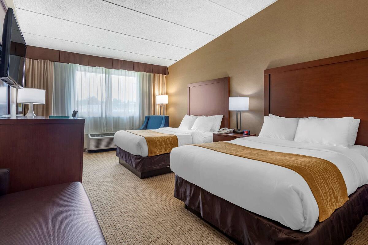 A hotel room with two beds, a desk, a chair, and a TV.