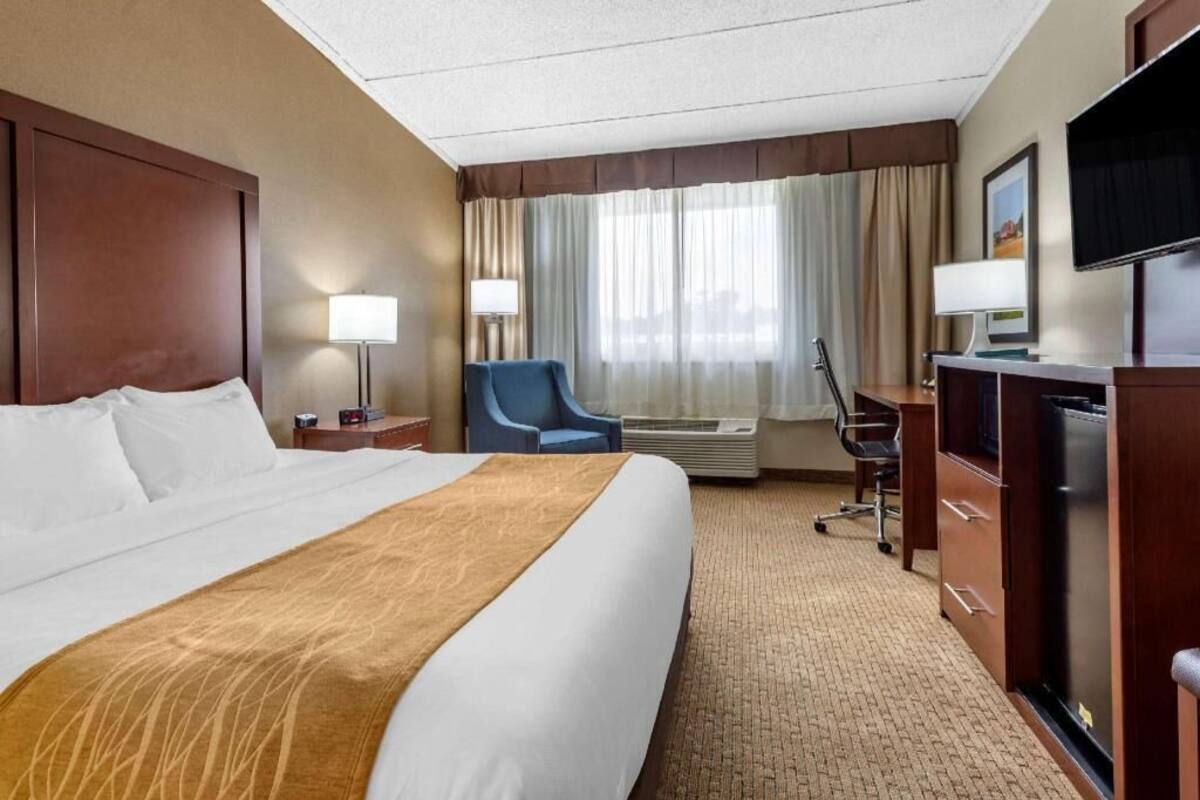 A hotel room with a large bed, a desk with a computer, a chair, and a TV.