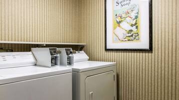 A laundry area with two washing machines and a dryer, a framed advertisement for Sunlight Soap, and a striped wall.