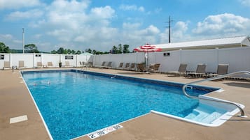 A rectangular pool with a blue water surface, surrounded by lounge chairs and umbrellas, and a white fence in the background.