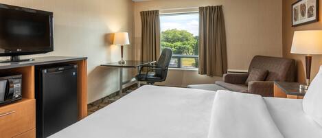 A hotel room with a bed, a desk with a chair, a television, a refrigerator, and a window with curtains.