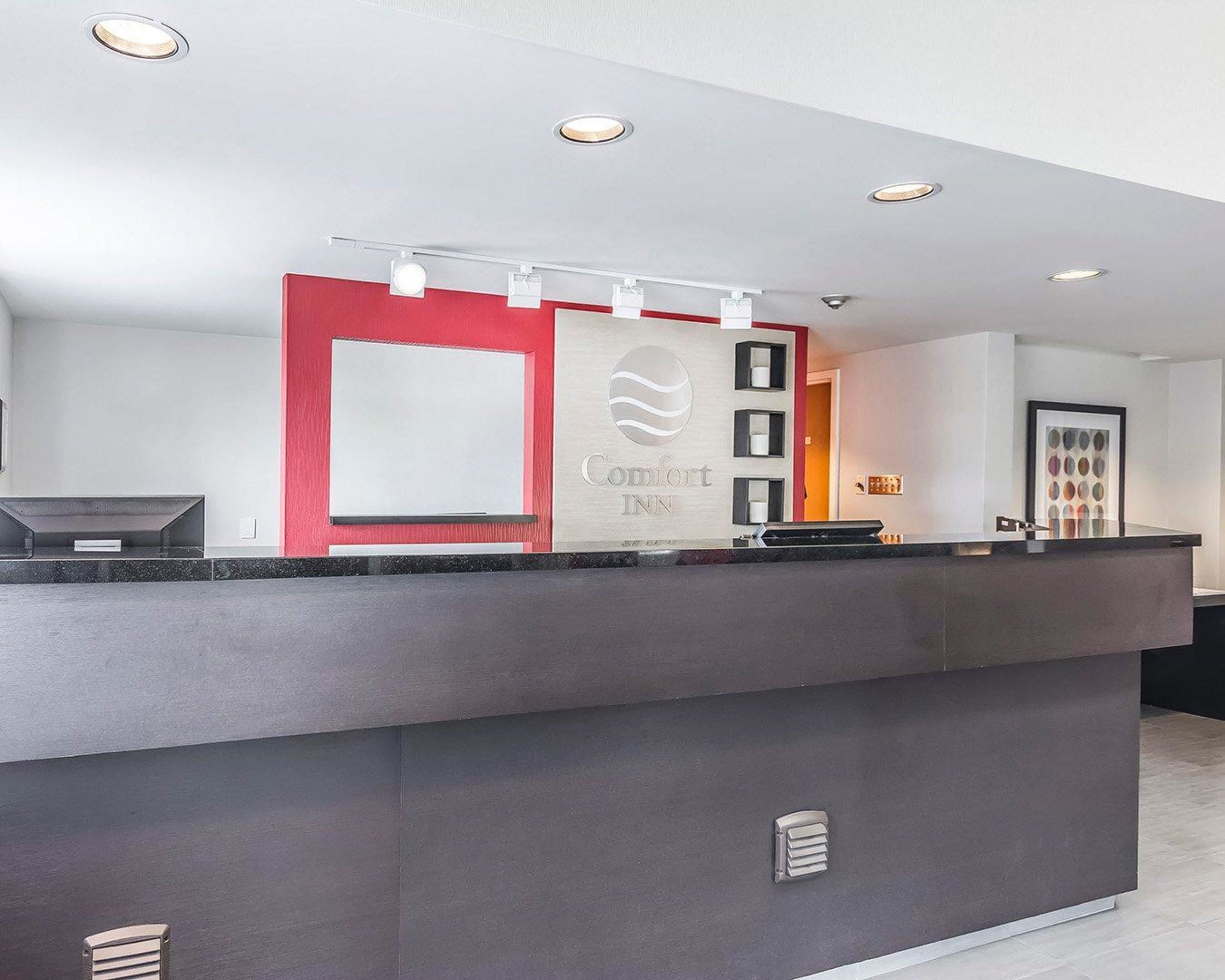 A modern reception desk with a red accent wall, a logo, and a framed artwork.