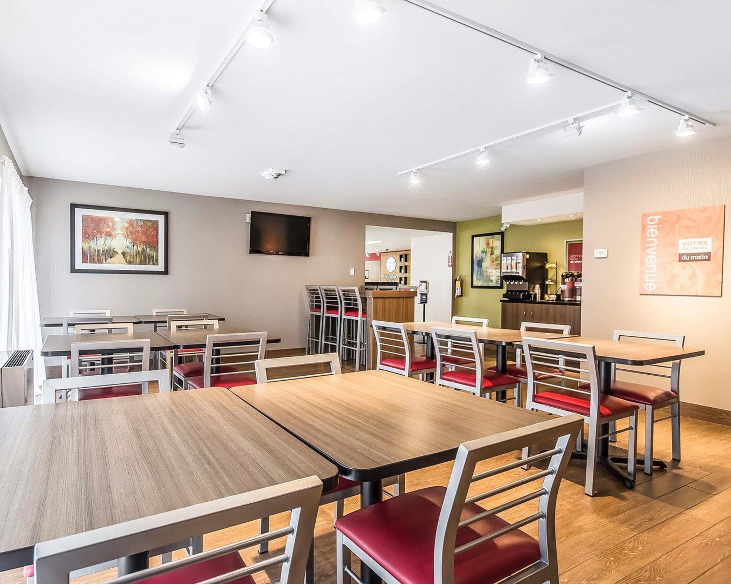 A modern dining area with multiple tables and chairs, a coffee machine, and a television on the wall.