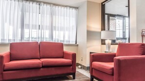 A modern hotel room with a red sofa, a smaller armchair, a lamp, and a large mirror.
