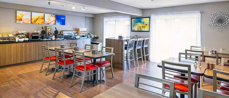 A modern dining area with wooden flooring, red cushioned chairs, and a central island with kitchen appliances.