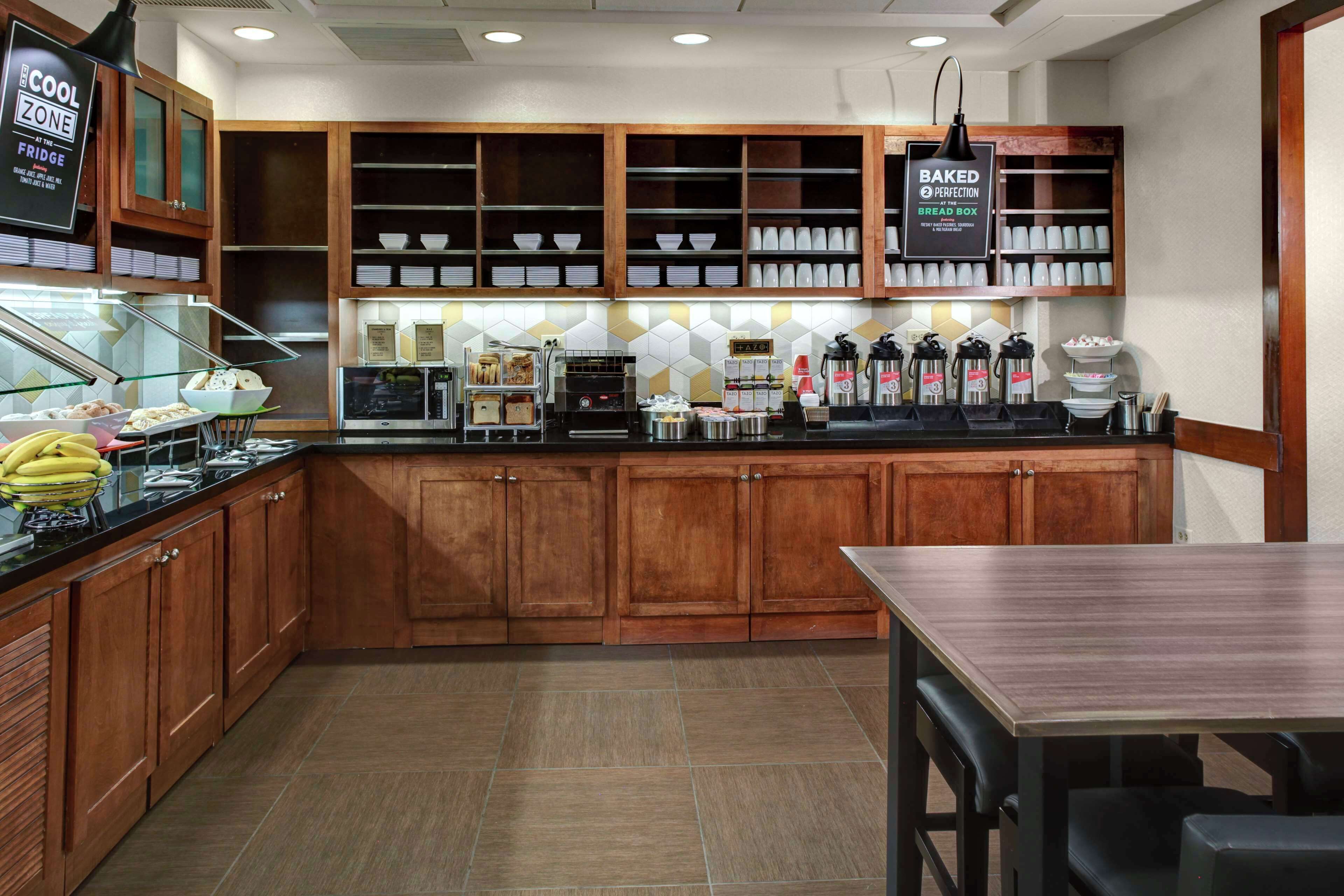 Una cocina con armarios de madera, una vitrina de vidrio con productos alimenticios y una estación de café con varias cafeteras.