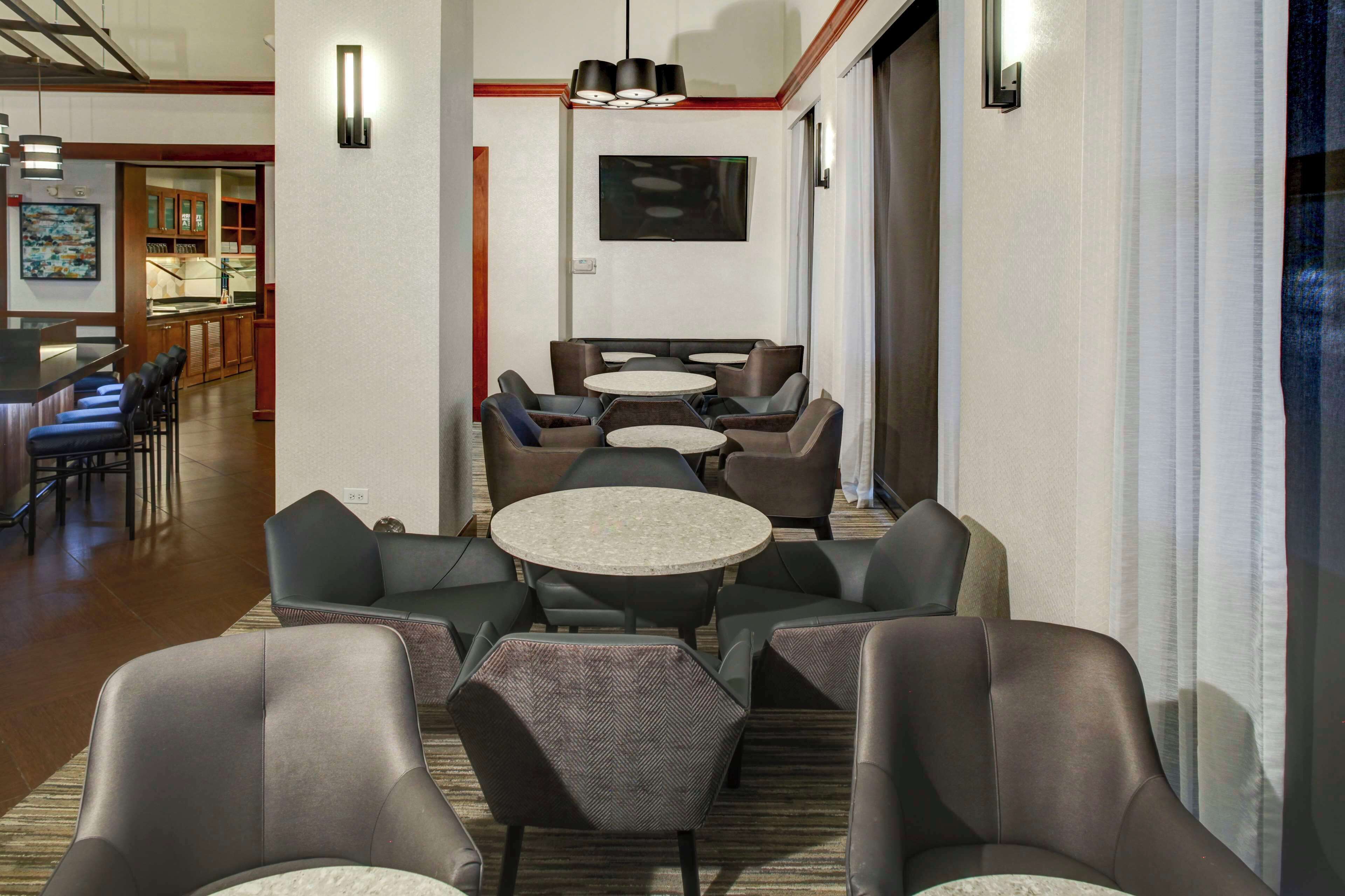 A hotel lobby with a bar area, multiple seating arrangements, and a television mounted on the wall.