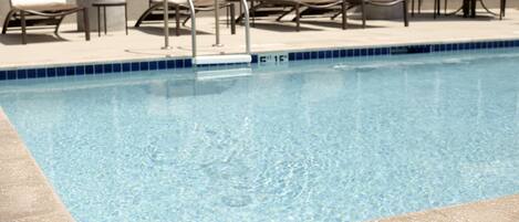 A swimming pool with clear water, surrounded by lounge chairs and a tiled deck.