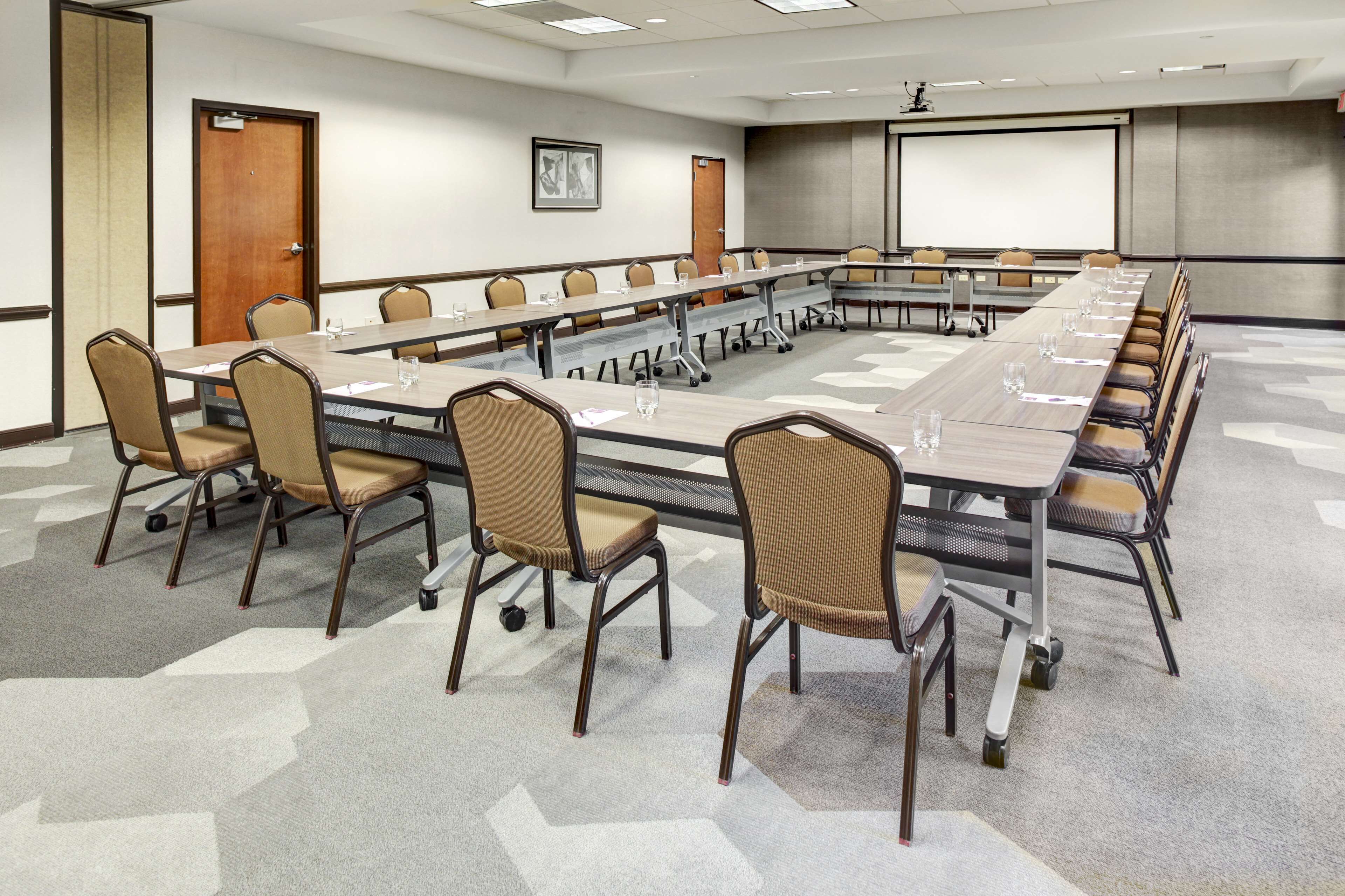 A conference room with a long table, chairs, a projector screen, and a carpeted floor.