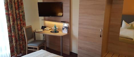 Habitación de hotel con una cama, un escritorio con un teléfono y una botella, un televisor montado en la pared y un armario.