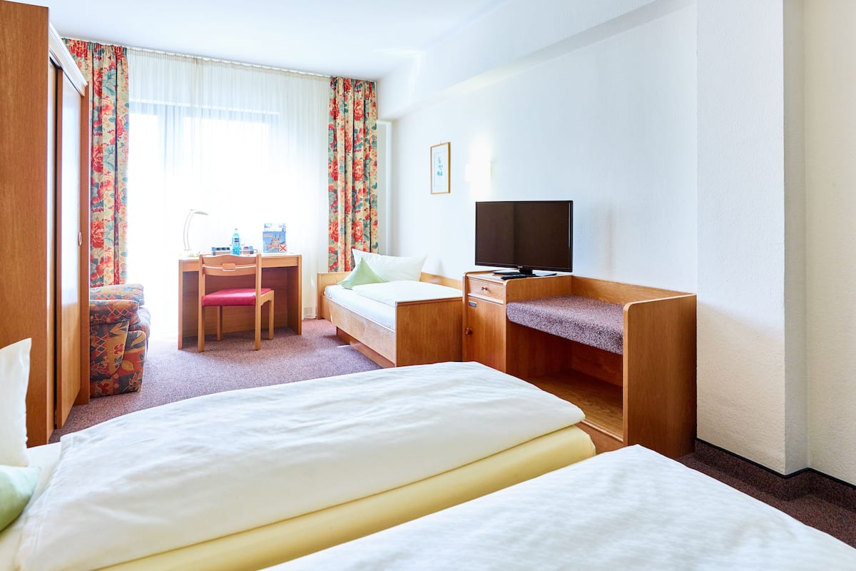 A hotel room with a bed, a desk with a chair, a television, and a window with curtains.