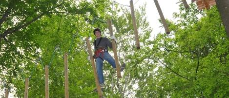 Una persona deslizándose en tirolesa por un área boscosa con postes y cuerdas de madera.