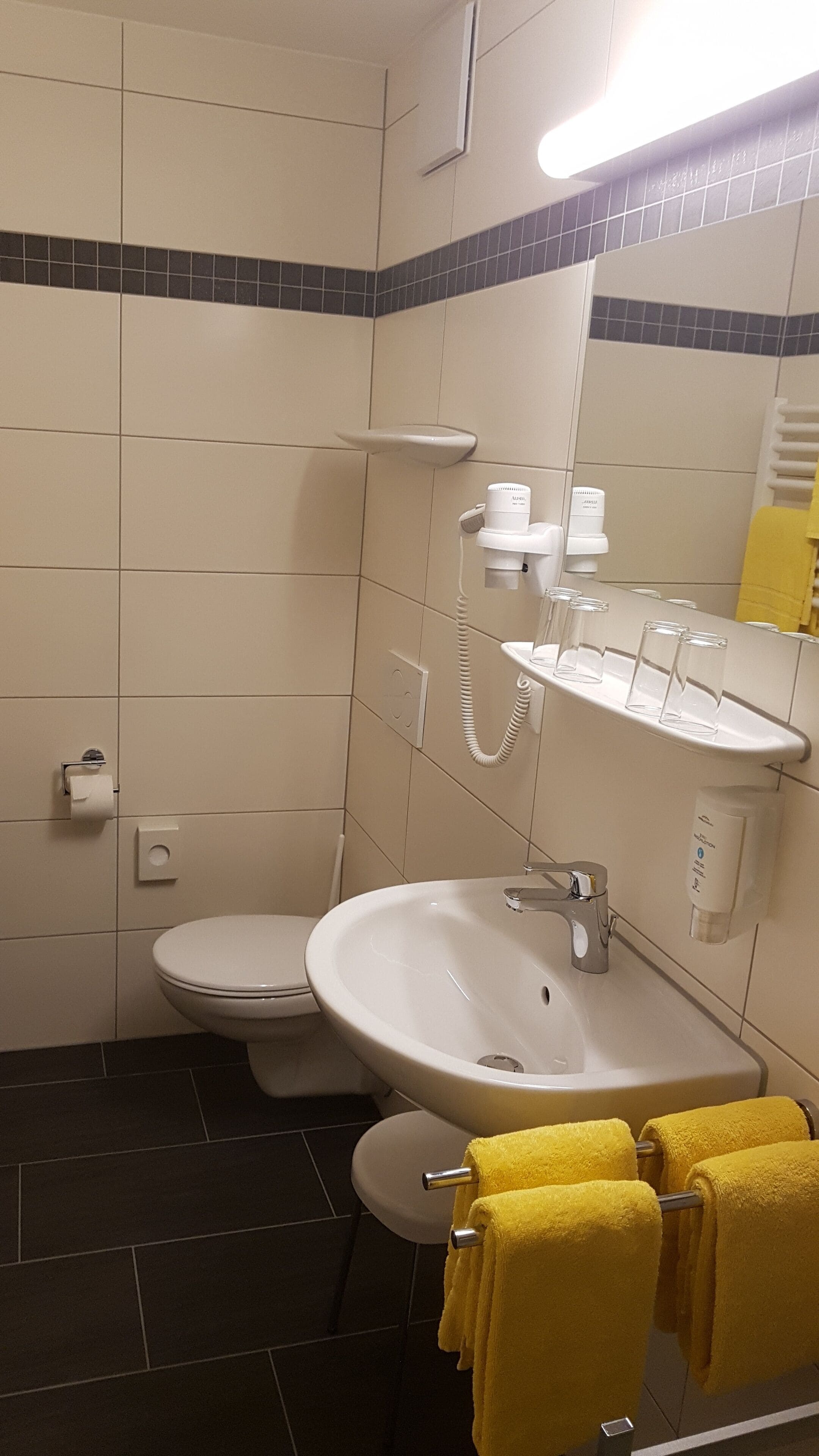 A bathroom with a toilet, sink, and mirror. There are towels hanging on a rack.