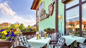 An outdoor seating area with tables and chairs, a flower planter, and a sign for Hotel Merian. - Hotel Merian Rothenburg (Rothenburg ob der Tauber)