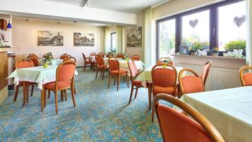 A dining area with tables and chairs, artwork on the walls, and a view of the outdoors through large windows.