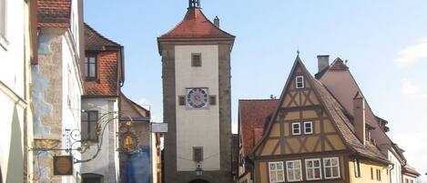 A cobblestone street with historic buildings, a prominent clock tower, and a sign reading "Goldener Hirsch Gastehaus".