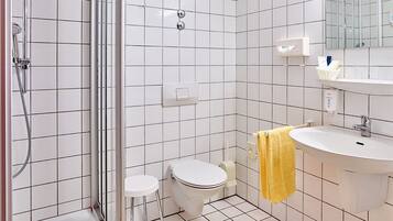 Un baño con azulejos blancos, ducha, inodoro, lavabo y espejo.
