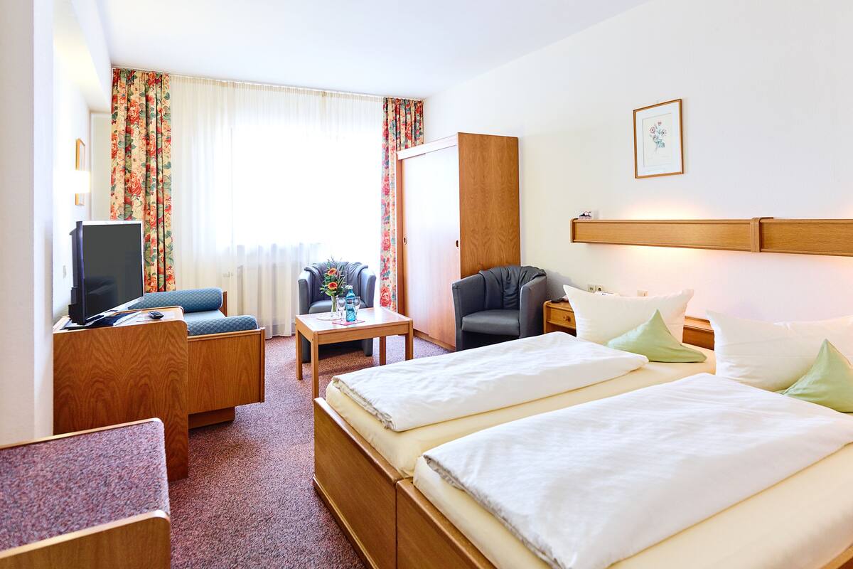 A hotel room with two beds, a desk, a chair, a television, and a window with curtains.