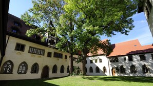 A courtyard with a large tree, a building with arched windows, and a red-roofed structure. - Hotel Merian Rothenburg (Rothenburg ob der Tauber)