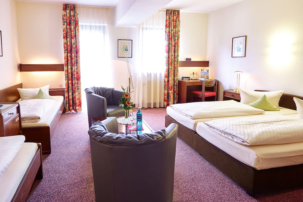 A hotel room with two beds, a desk, a chair, a TV, and a small table with a vase and a bottle.