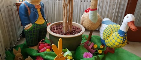 A room with a large potted plant, a wooden duck, a rabbit, and a duck figurine.