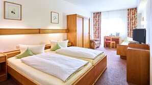A hotel room with two beds, a desk, a chair, a television, and a wardrobe. - Hotel Merian Rothenburg (Rothenburg ob der Tauber)