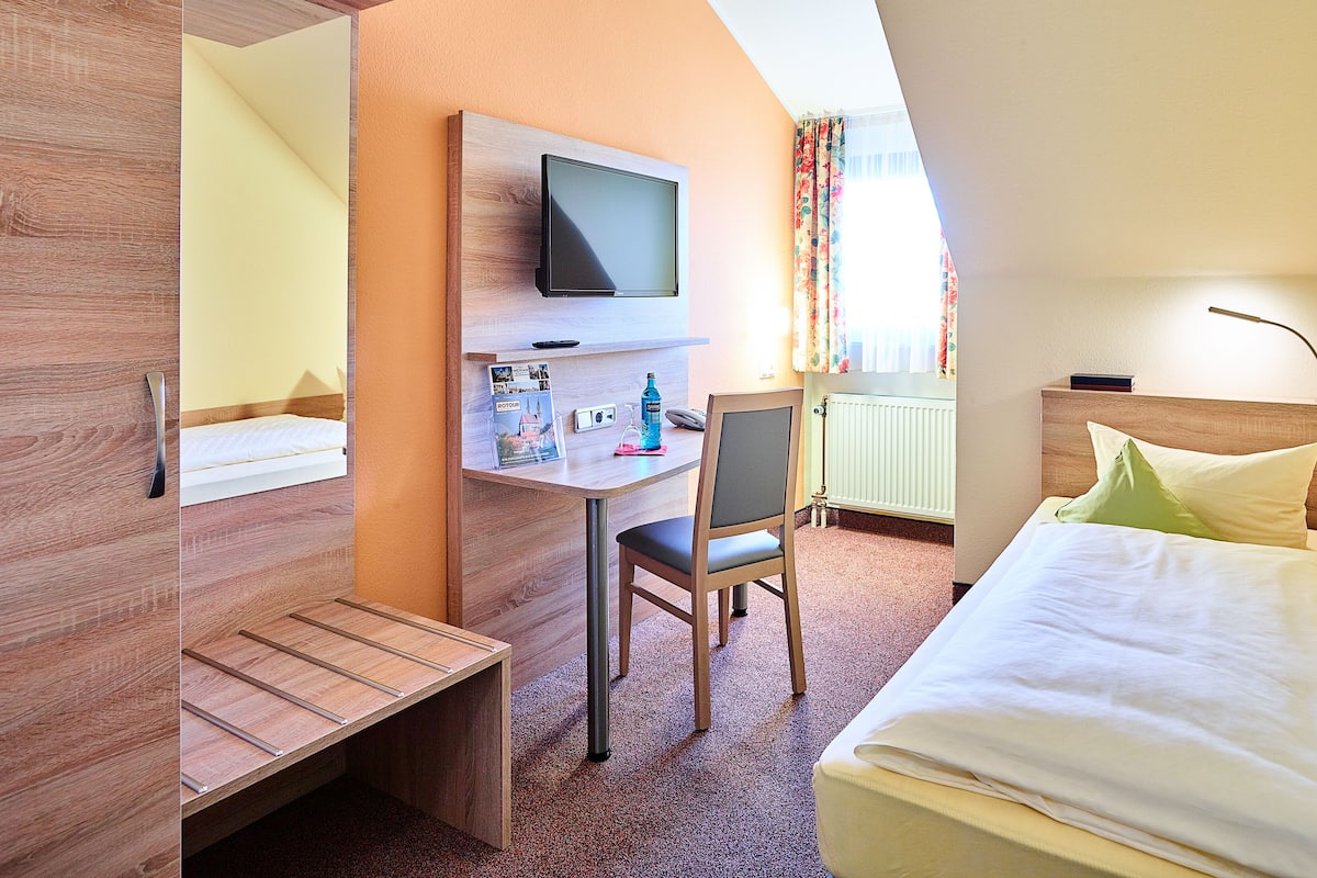 A hotel room with a bed, a desk with a chair, a television, and a window with curtains.