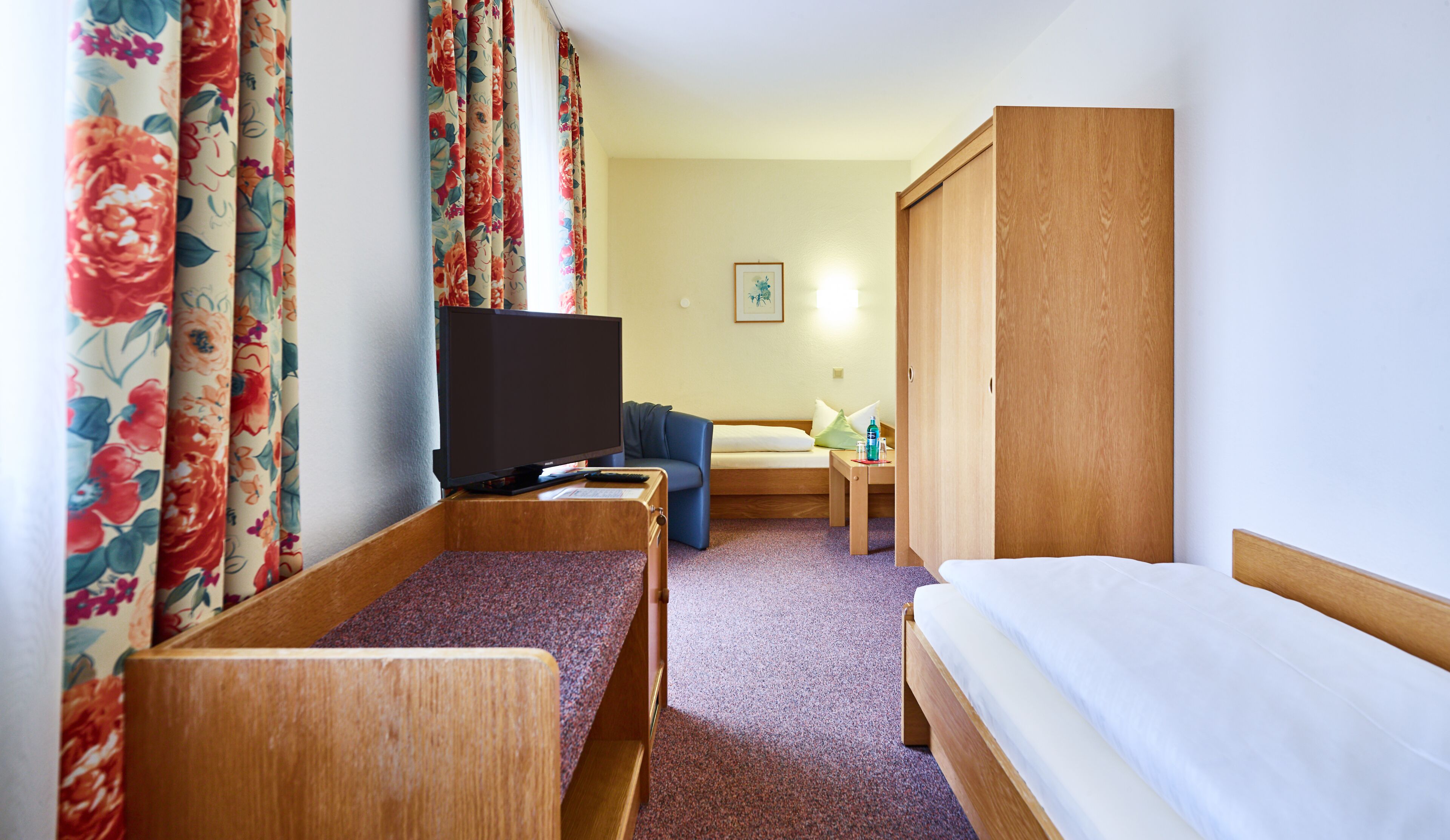 A hotel room with a bed, a TV, a sofa, and a wooden wardrobe.