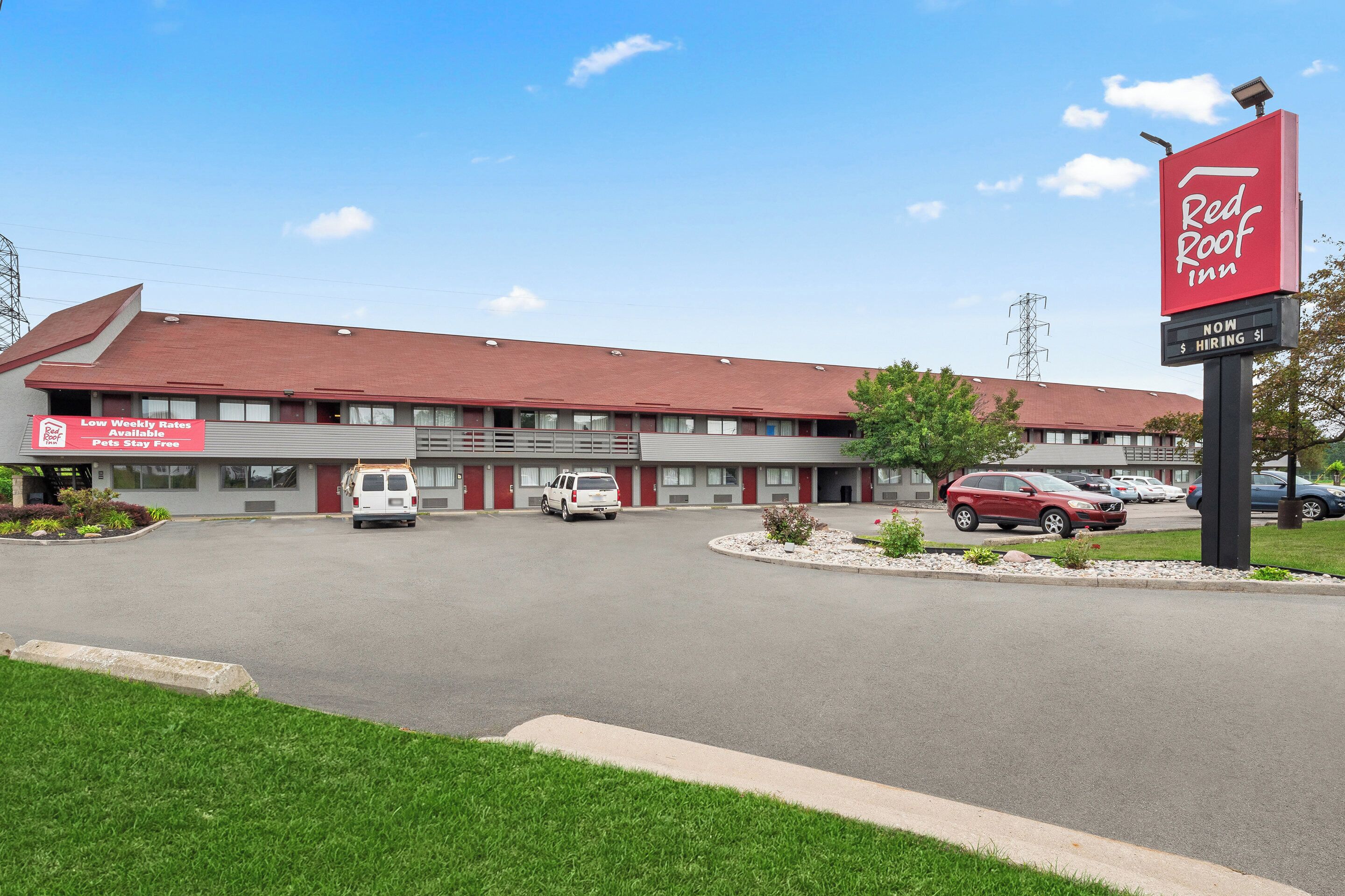 A Red Roof Inn with a parking lot, a red sign, and a building with a red roof.