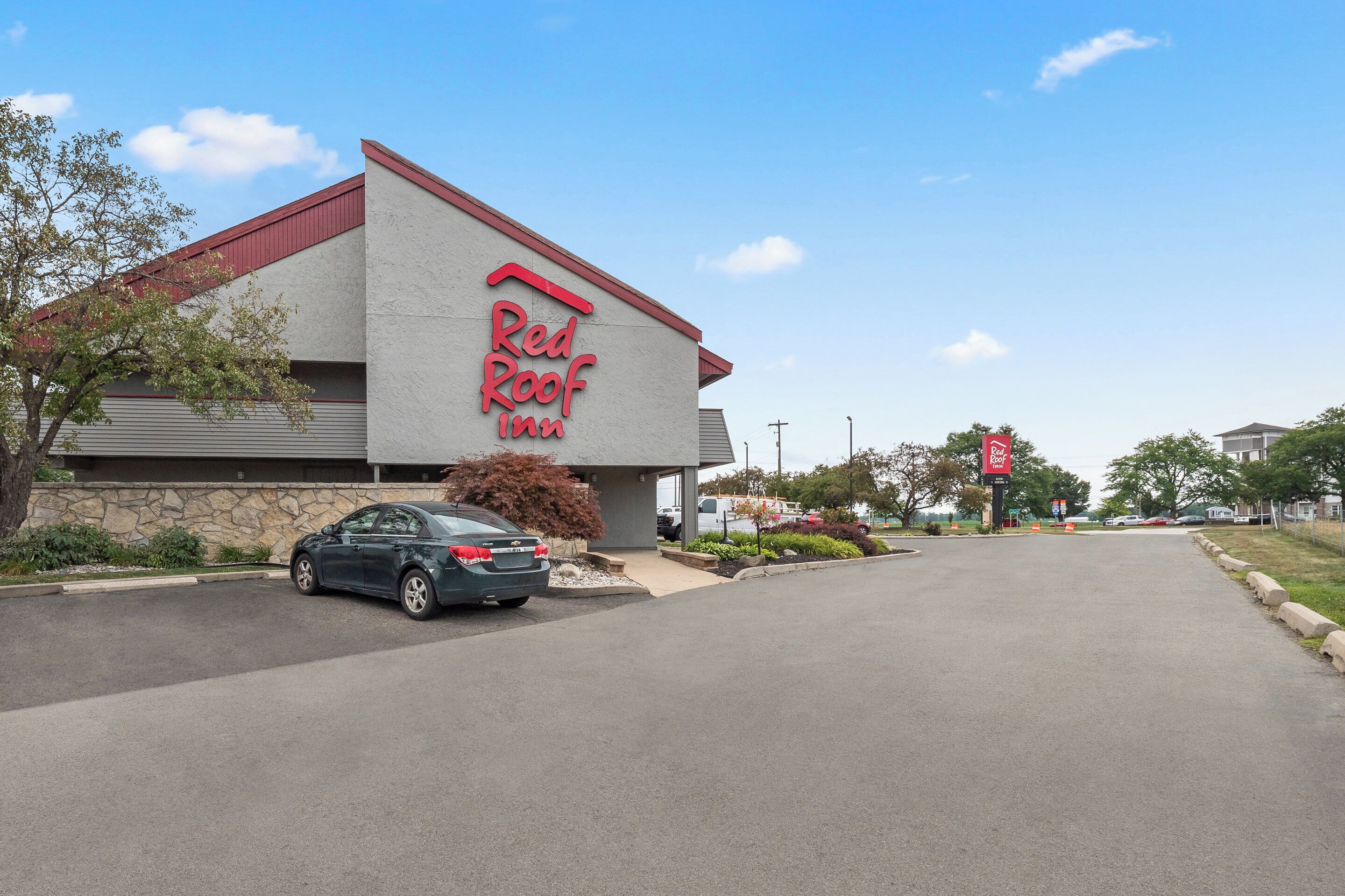 A Red Roof Inn with a modern design, a parking lot, and a clear sky.