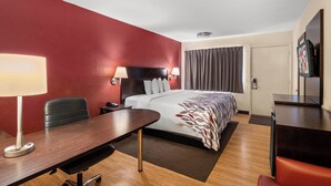 A hotel room with a bed, a desk, a chair, a TV, and a lamp. - Red Roof Inn Lansing East – MSU (Lansing)
