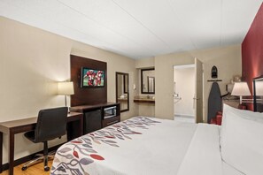 A hotel room with a bed, desk, television, and a bathroom door. - Red Roof Inn Lansing East – MSU (Lansing)